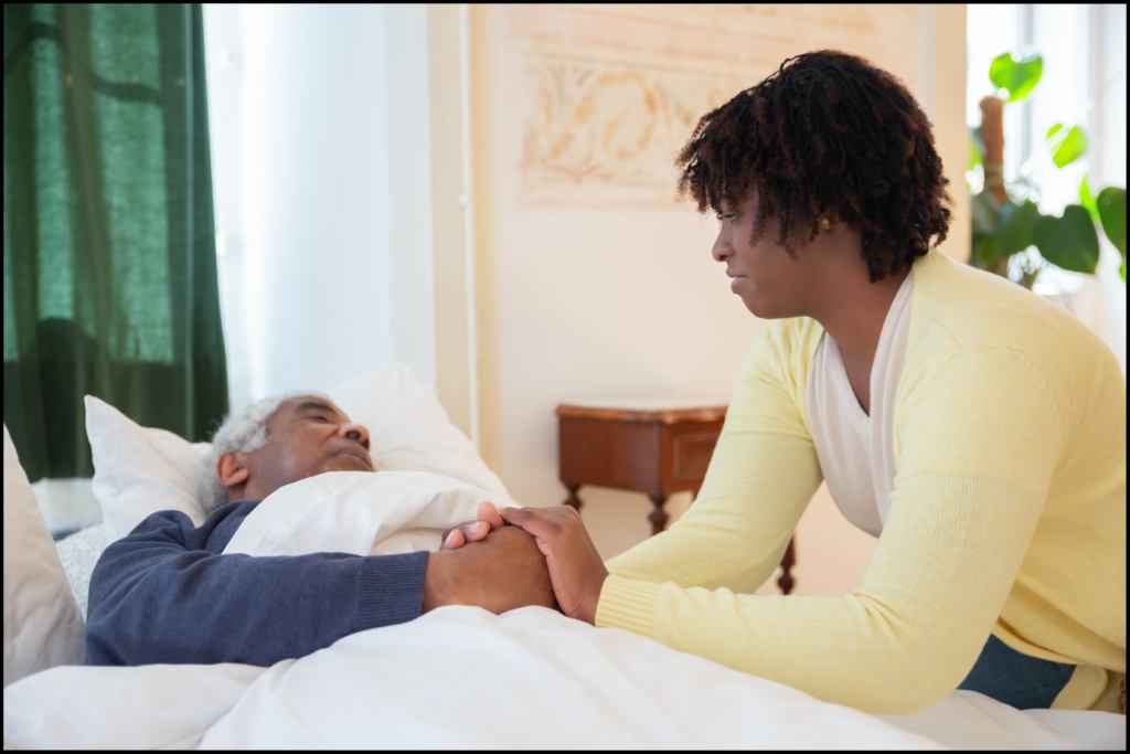 A woman holding a man’s hand while he sleeps